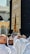 A group of people dressed in white robes gather around the Kaaba, a cube-shaped structure draped in black cloth with gold Arabic script. The scene captures the spiritual atmosphere of a holy place with architectural elements visible in the background.