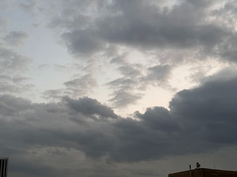 Dark clouds spread across the sky with patches of lighter areas visible behind them, suggesting an overcast or stormy weather condition. A portion of a building with a few antennas is present in the lower right corner.