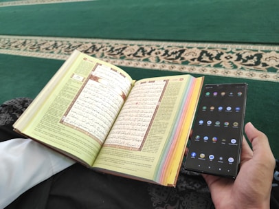 A person reading the Quran on a tablet, surrounded by notes and a cup of tea.