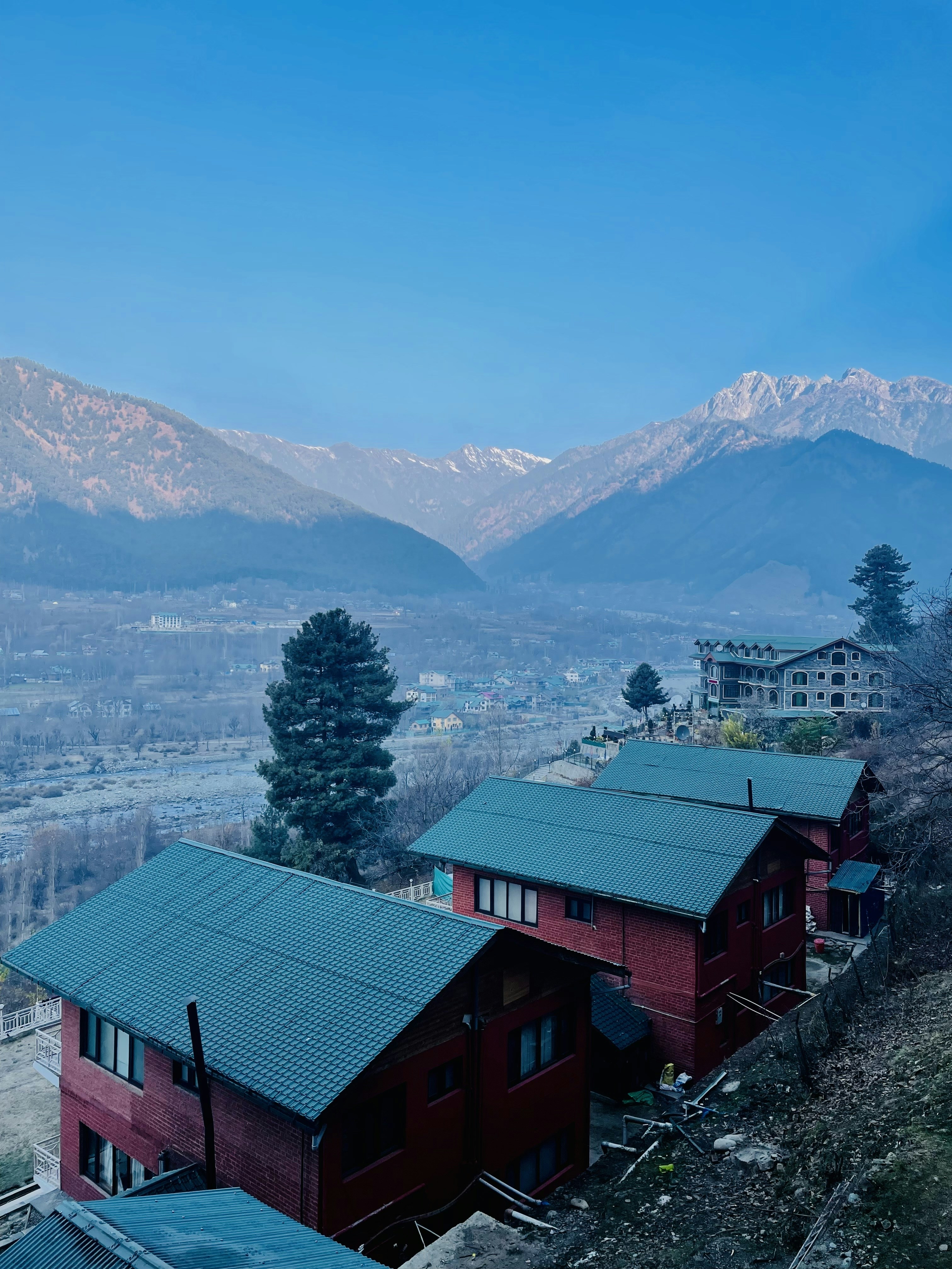 a red building with a green roof and mountains in the background
