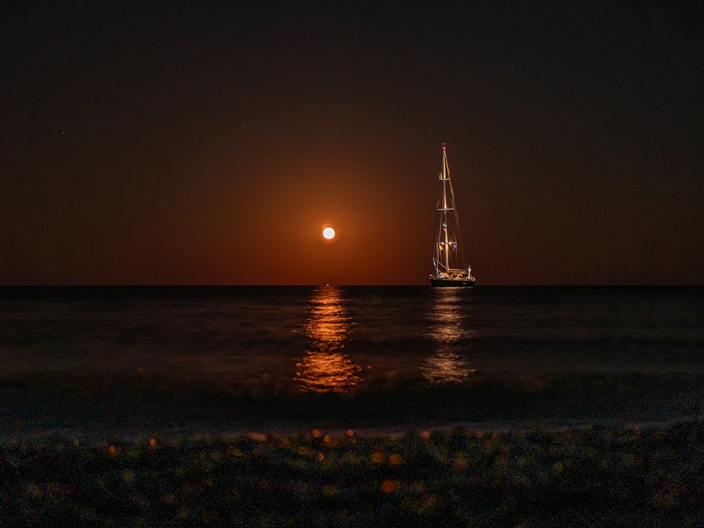 a sailboat in the ocean at night with a full moon in the background
