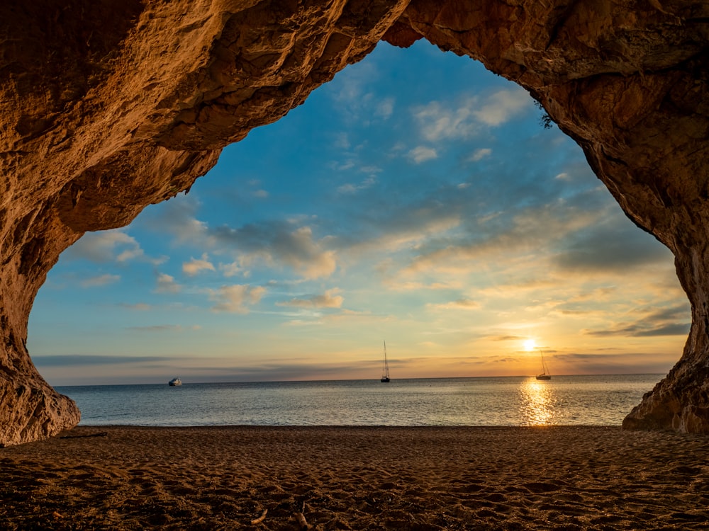 the sun is setting in a cave on the beach