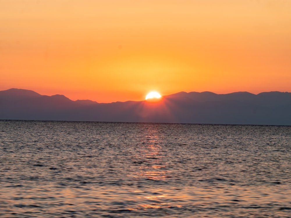 the sun is setting over the ocean with mountains in the background