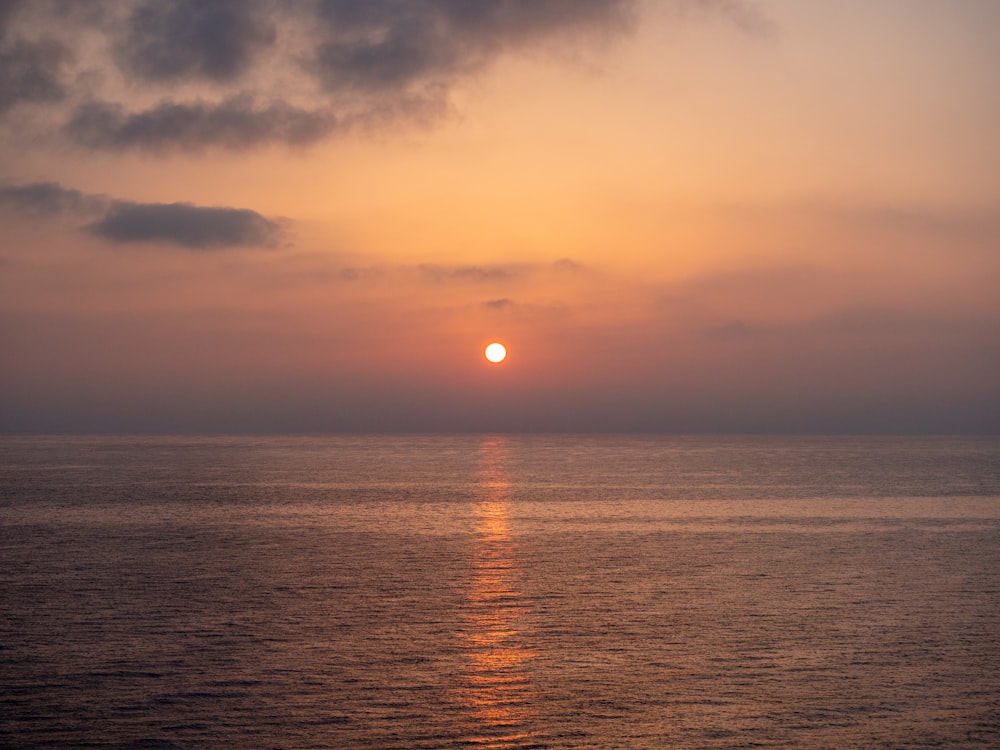 the sun is setting over the ocean on a cloudy day