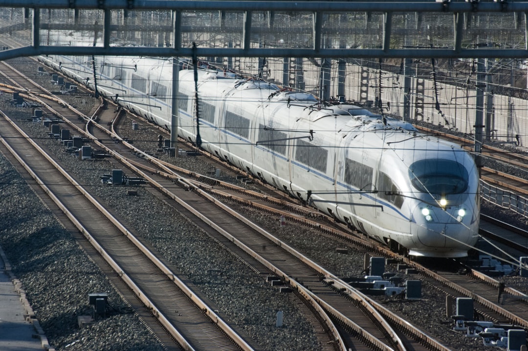 a silver train traveling down train tracks next to a station,