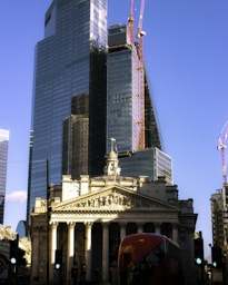 a red double decker bus driving past a tall building