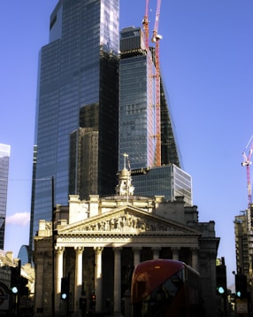 a red double decker bus driving past a tall building