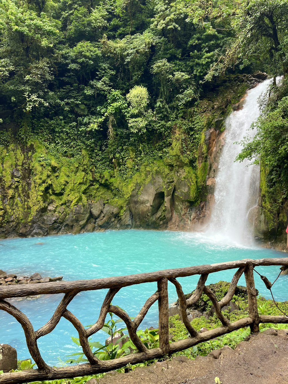 a woman standing on a bridge looking at a waterfall