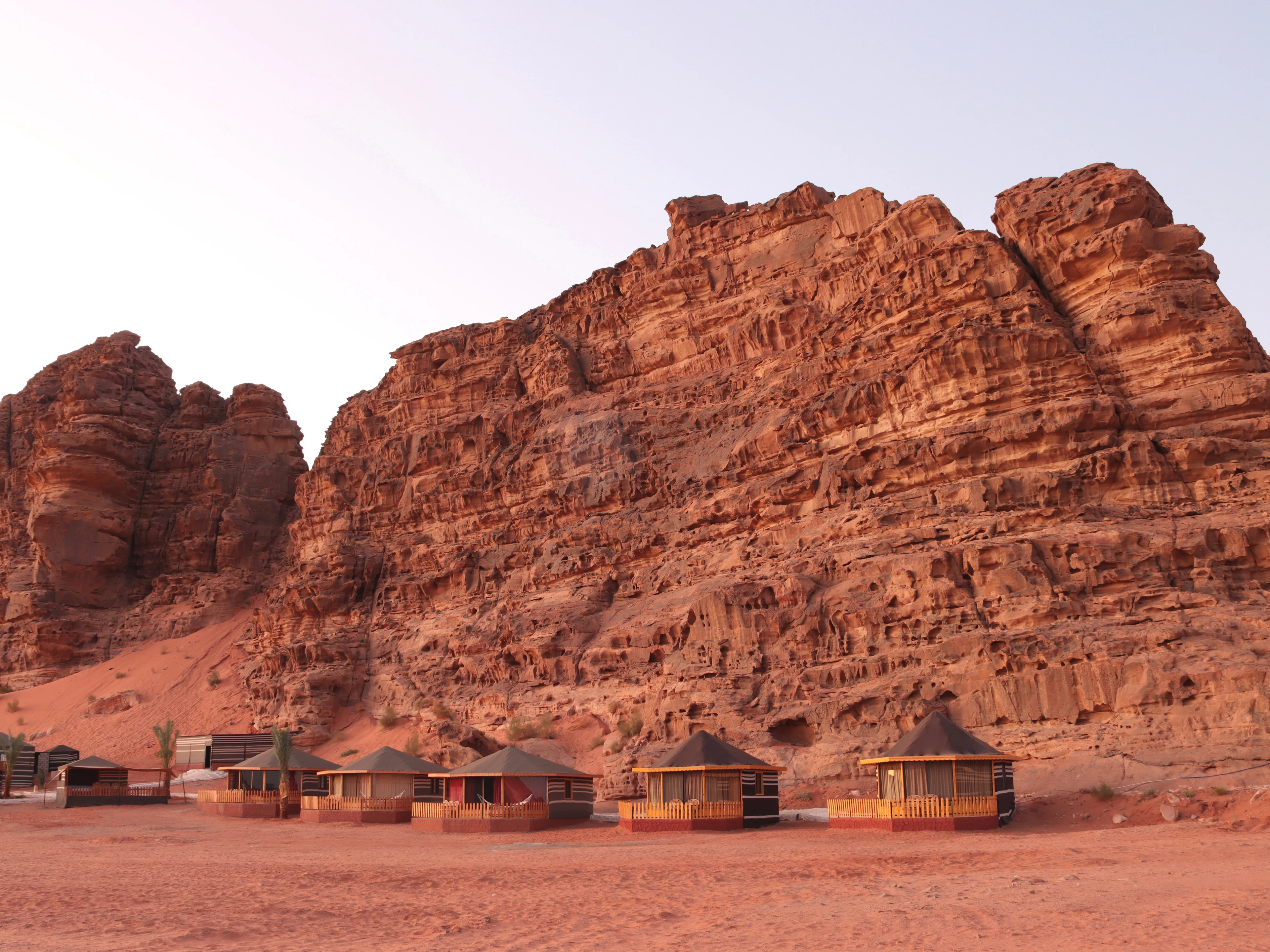 Round camp huts on red sand beneath a wall of sandstone cliffs in Wadi Rum