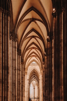 A majestic view of a cathedral interior featuring soaring Gothic arches and intricate stone columns. The symmetry and depth create a sense of awe, capturing the grandeur of the architecture with warm, ambient lighting that casts gentle shadows along the stone surfaces.