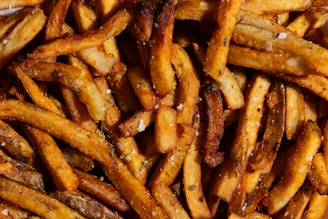 Close-up of golden, crispy fries sprinkled with fresh herbs on a rustic wooden table.