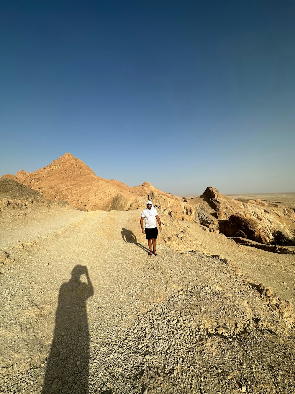 a man walking down a dirt road in the desert