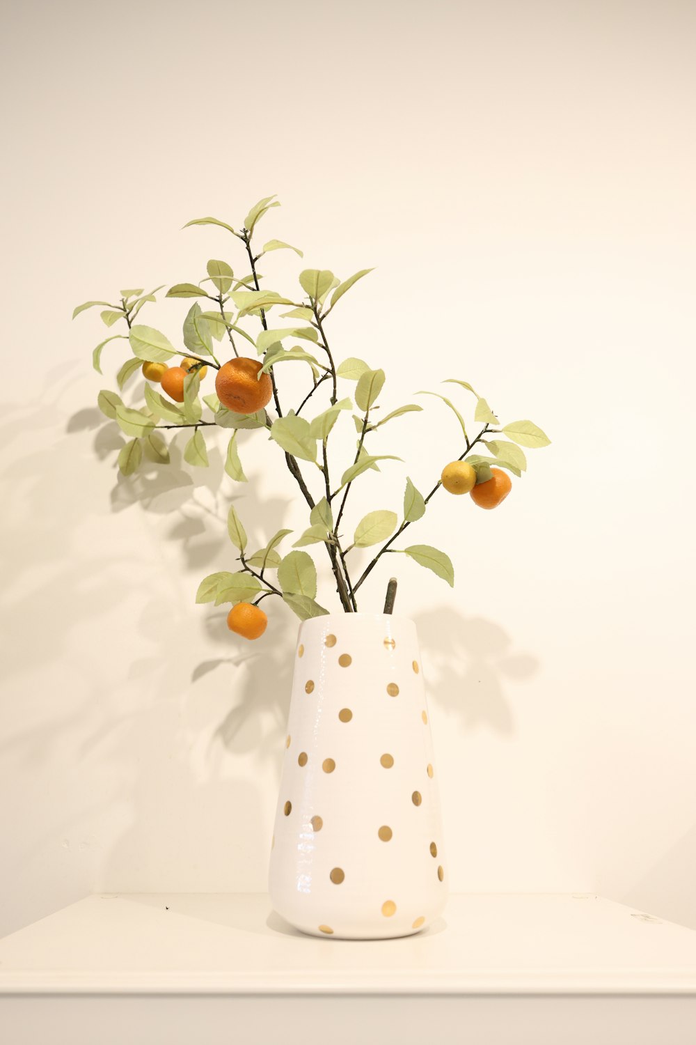 a white vase filled with oranges on top of a white shelf