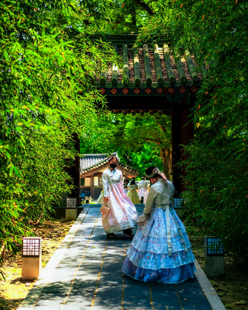 a couple of women in long dresses walking down a path