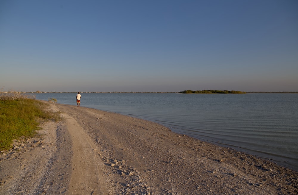 a person standing on a dirt road next to a body of water