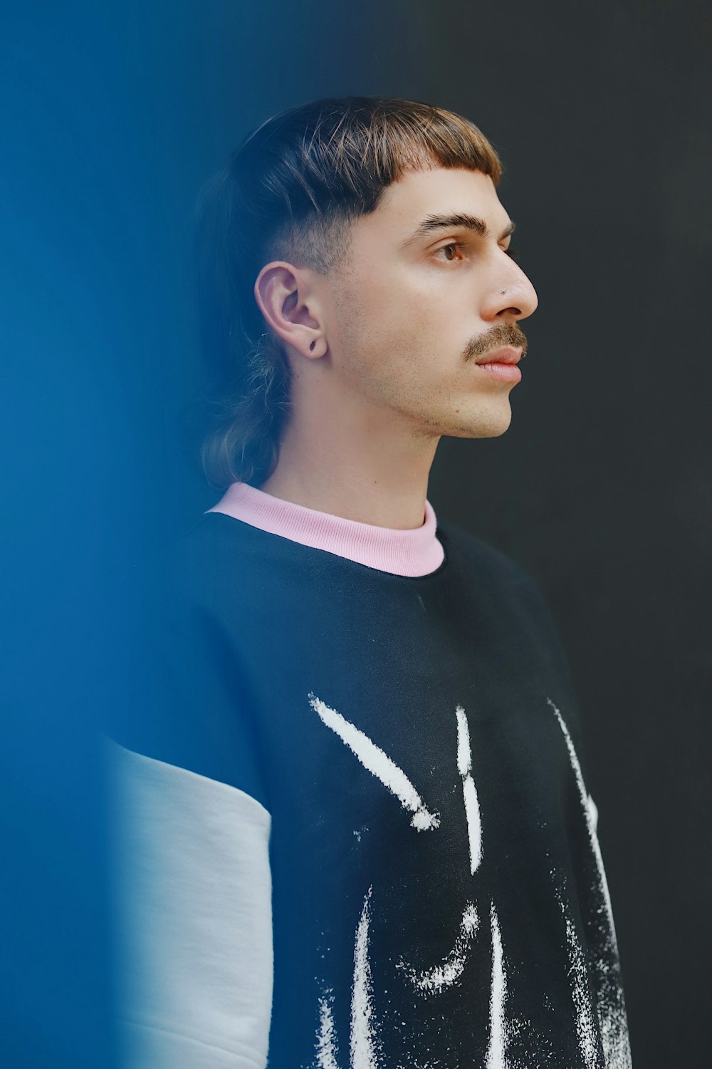 un homme avec une moustache debout devant un mur bleu