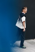 A person with short hair and a mustache is wearing a fashionable oversized shirt with a graphic design and dark pants. The setting is minimalistic with a blue and black background, adding a modern artistic touch.