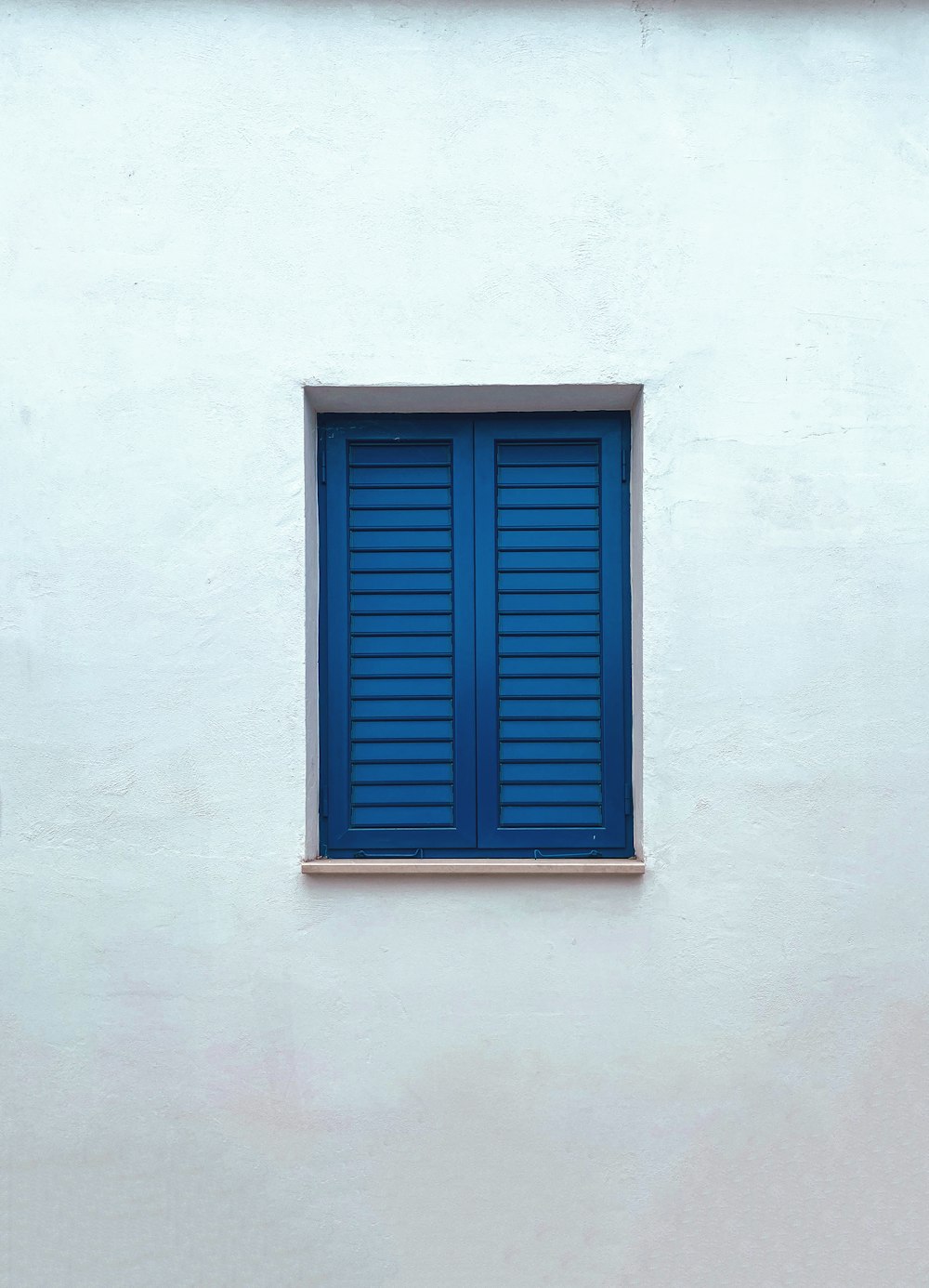 a white building with a blue window and a bench in front of it