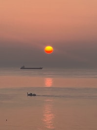 A large tanker ship loaded with oil navigating through calm international waters at sunset.