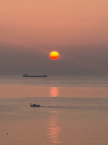 A large tanker ship loaded with oil navigating through calm international waters at sunset.