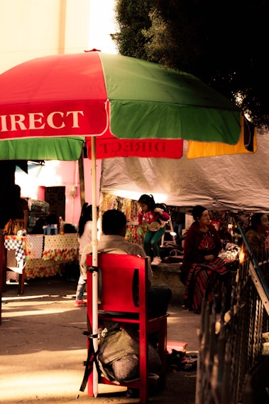 A vibrant street scene in Cameroon showing locals engaged in lively discussion under colorful market umbrellas.