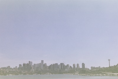 A city skyline with a prominent tower on the right side against a vast, clear sky. The skyline is positioned above a body of water, with various buildings of different heights.