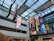 An indoor atrium with a glass ceiling showcasing multiple vertical banners hanging from the roof. The banners display various colorful graphics, including video game and technology logos such as Xbox and Godot Foundation, and animated characters. The building interior is modern with white walls and multiple floors visible.