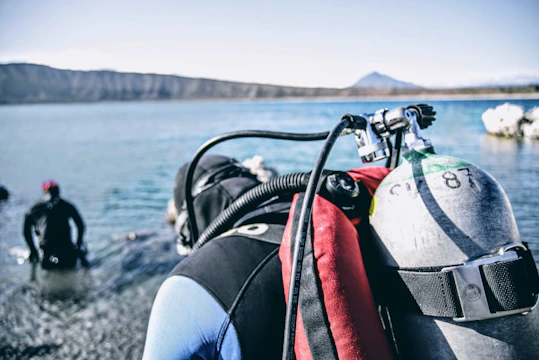 A group of divers preparing their gear on a rocky shore under a clear sky.