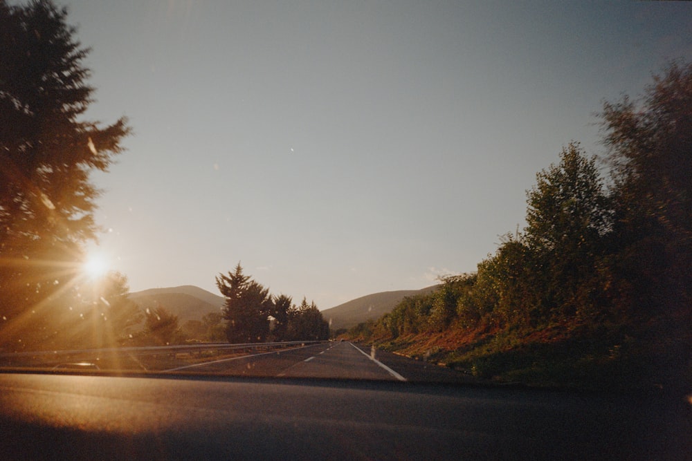 the sun is shining through the trees on the side of the road