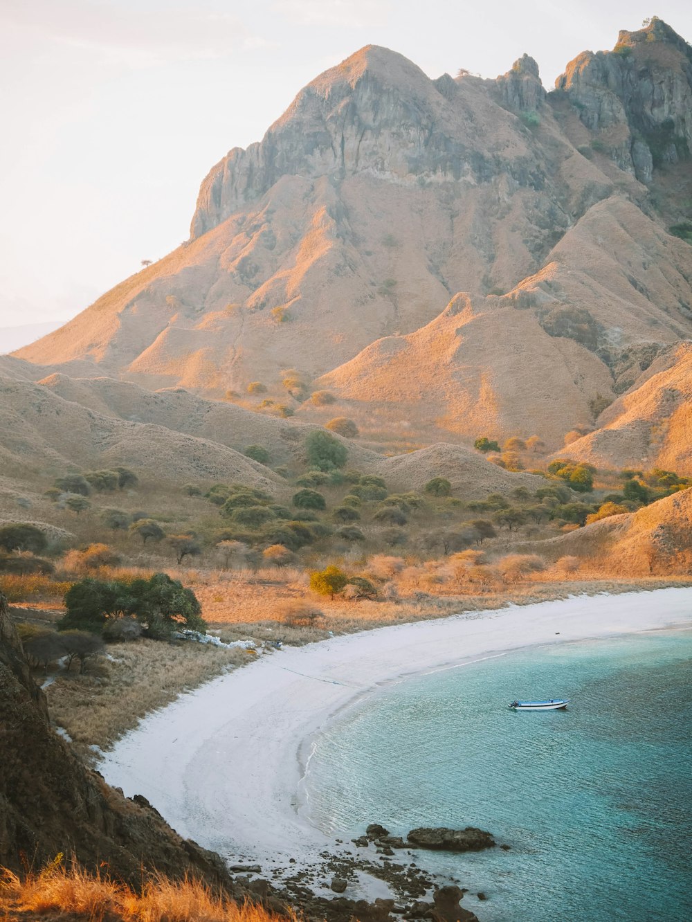 a beach with a boat in the water and a mountain in the background