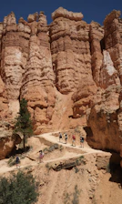 A smiling tour guide pointing out a stunning red rock formation to a small group of hikers under a bright blue sky.