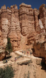 Hikers trekking along a narrow path with towering desert cliffs glowing in deep red light.