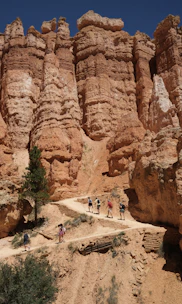 Hikers trekking along a narrow path with towering desert cliffs glowing in deep red light.