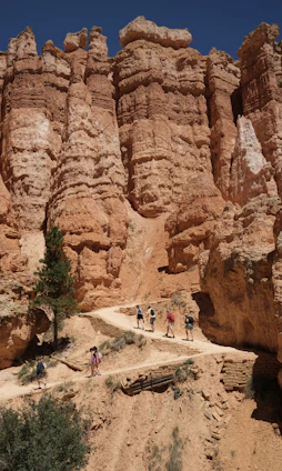 A smiling tour guide pointing out a stunning red rock formation to a small group of hikers under a bright blue sky.