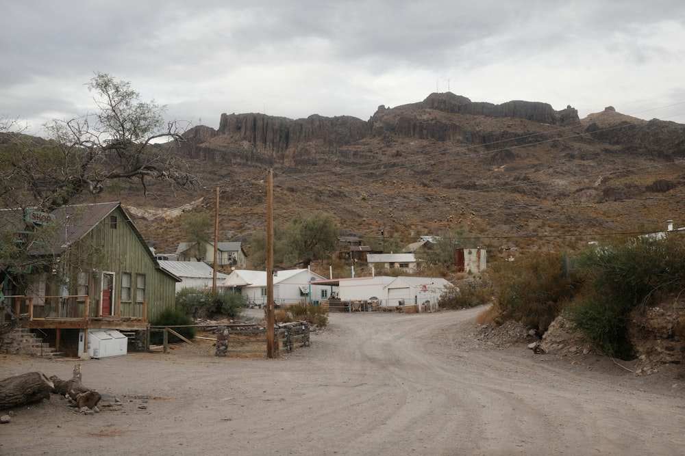 a dirt road with houses and mountains in the background