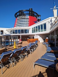 a cruise ship deck with lounge chairs and a large cruise ship in the background