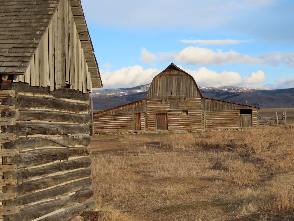 an old barn in a field with mountains in the background