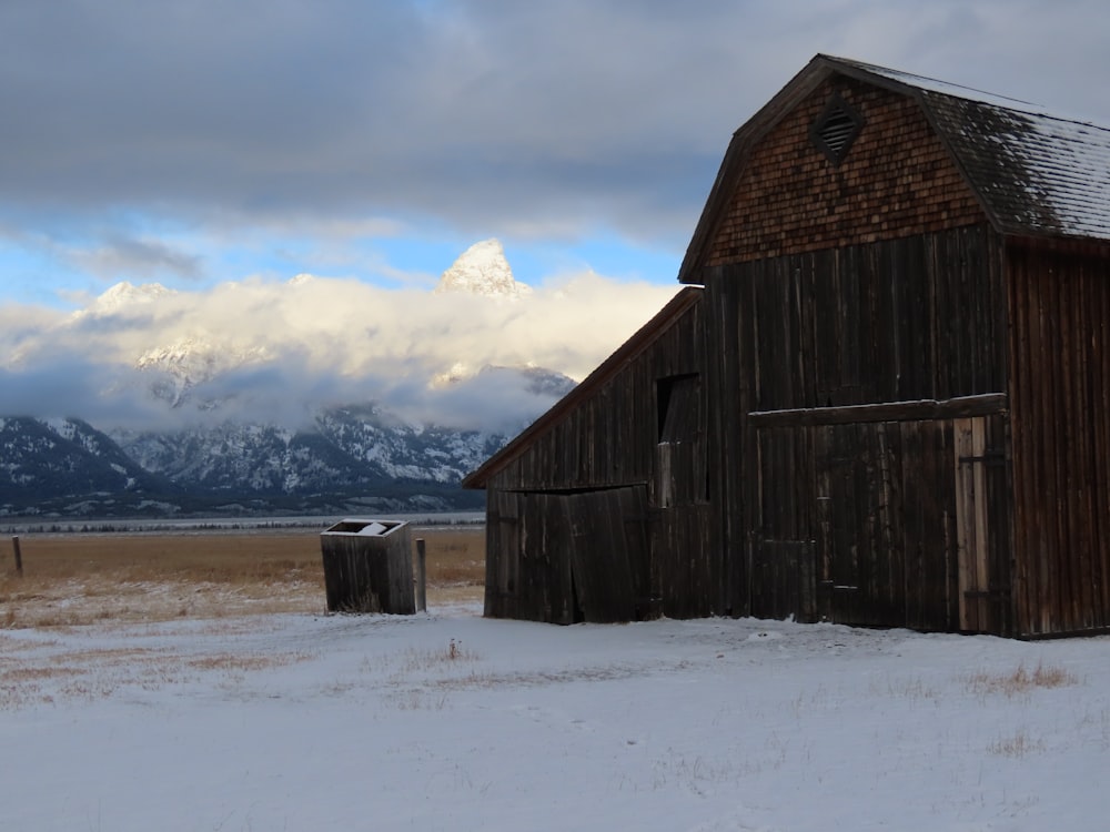 a barn in a snowy field with mountains in the background