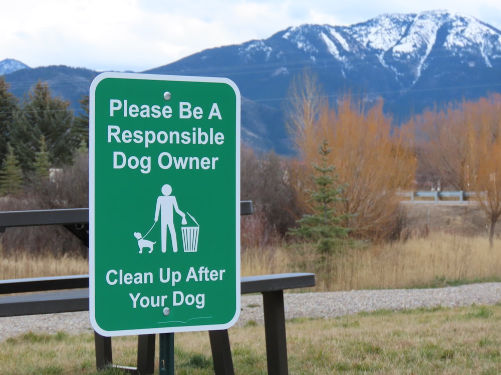 a green sign on a wooden bench in front of a mountain