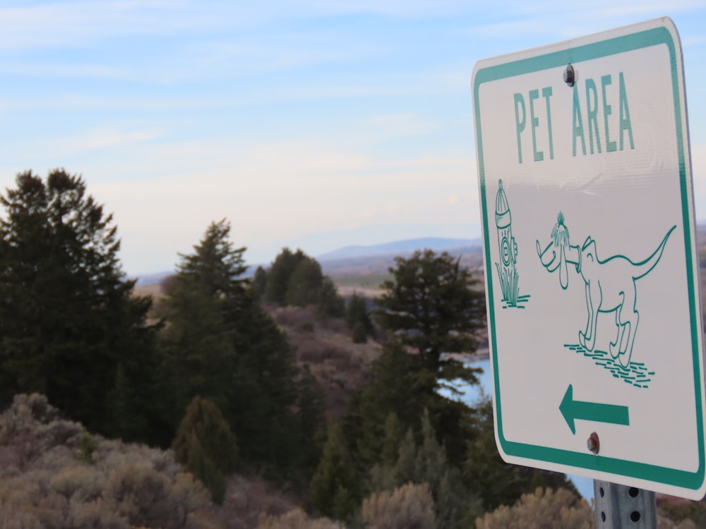 a green and white pet area sign with trees in the background