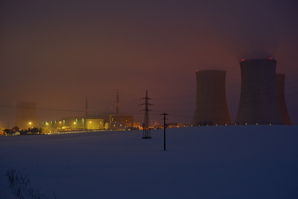 a snowy field with power lines and power plant in the background