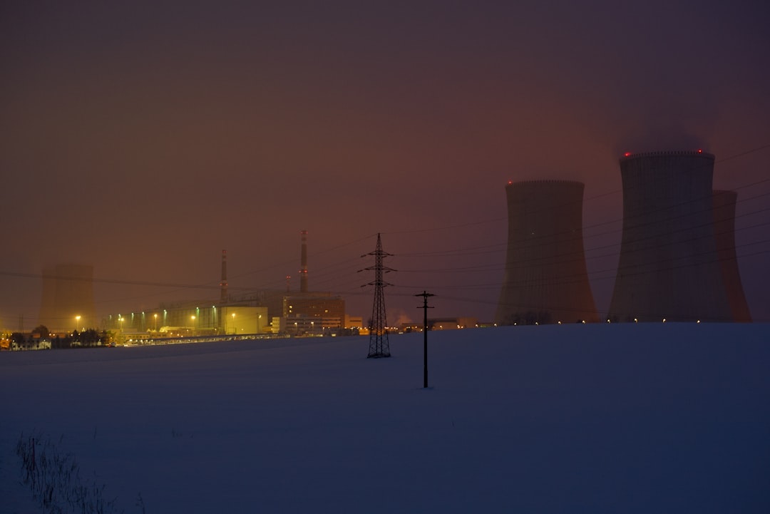 a snowy field with power lines and power plant in the background,