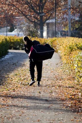 Model carrying a Helms satchel walking through a leafy park in autumn.