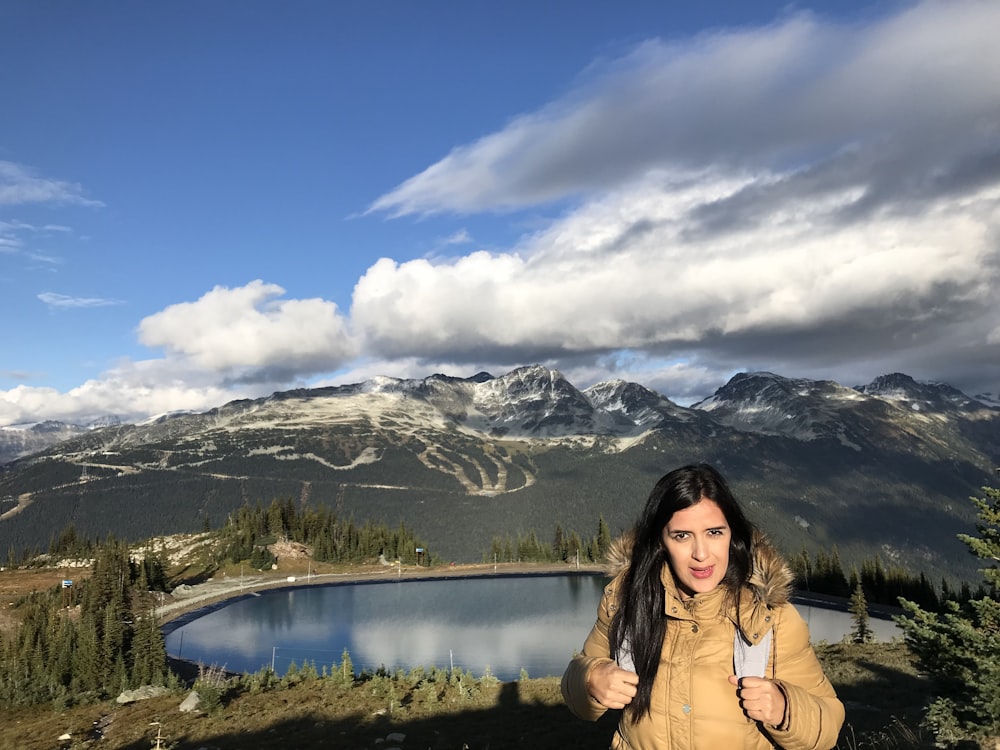 a woman standing in front of a lake with mountains in the background