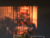 Wooden plaques are mounted on a wall, displaying words like 'Dios', 'Gracia', 'Amor', 'Familia', and more in Spanish. Sunlight casts warm shadows across the wall, enhancing the cozy atmosphere.