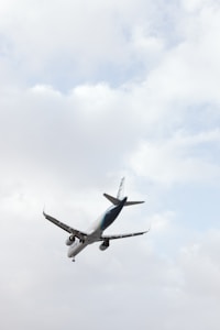 An aircraft is captured in mid-air against a backdrop of a cloudy sky. The angle of the photo emphasizes the airplane's underside, with the wings and engines clearly visible.