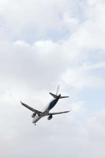An aircraft is captured in mid-air against a backdrop of a cloudy sky. The angle of the photo emphasizes the airplane's underside, with the wings and engines clearly visible.