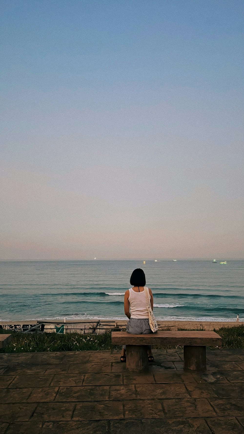 a woman sitting on a bench looking out at the ocean