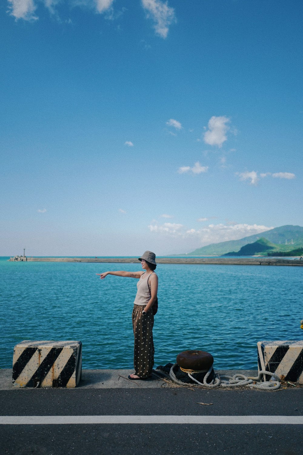 a woman standing on the side of a road next to a body of water