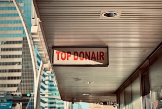 A sign reading 'Top Donair' hangs under a building canopy in an urban area, with modern high-rise buildings visible in the background.